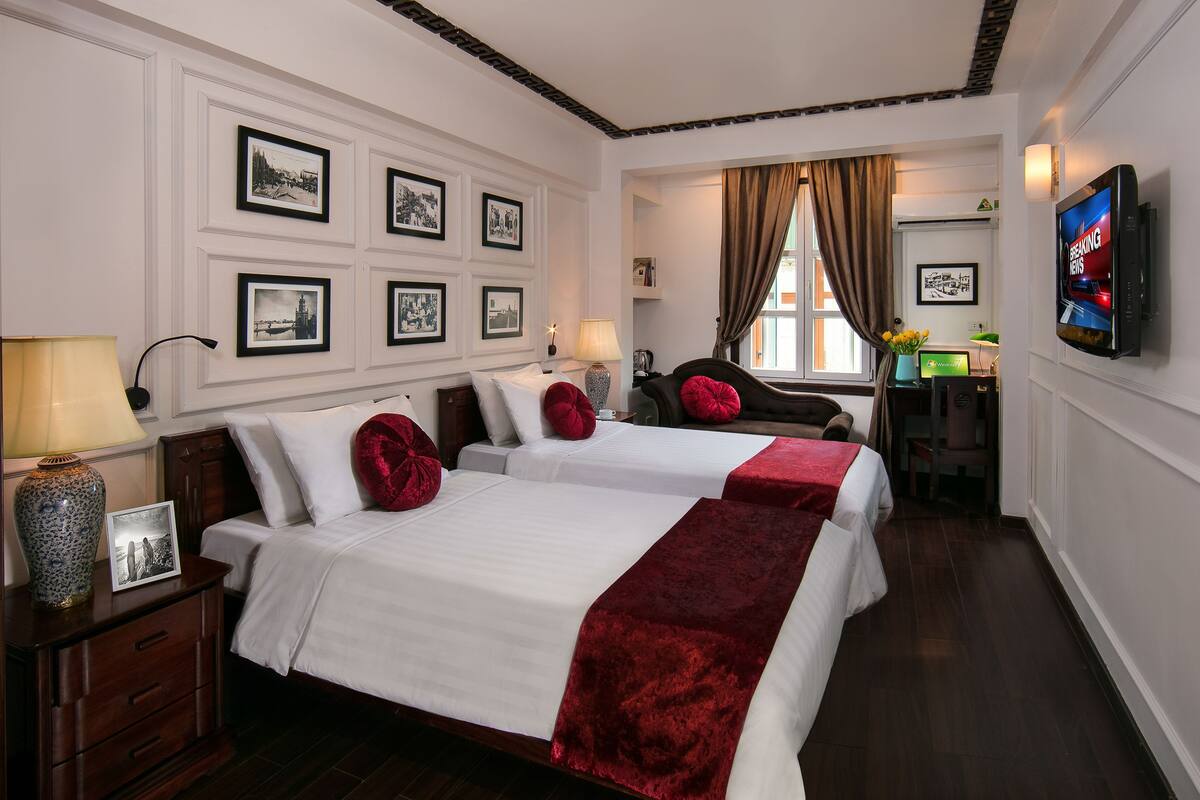A hotel room with two beds, a TV, a desk with a computer, and framed pictures on the wall.