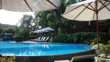 Une piscine entourée de chaises longues et de parasols, elle-même bordée d’une végétation luxuriante et d’une cascade.
