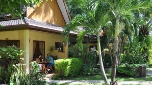 A yellow building with a tiled roof, surrounded by lush greenery and palm trees. - Palm Garden Resort (Rawai)