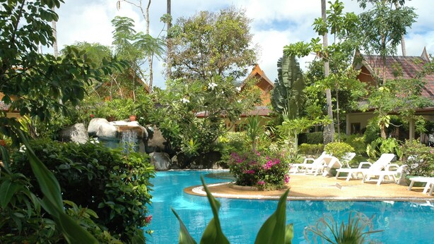 A pool surrounded by lush greenery and a small waterfall, with lounge chairs and a building in the background. - Palm Garden Resort (Rawai)