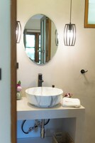A bathroom with a round mirror, a white sink, and two pendant lights.