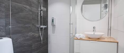 Un baño moderno con cabina de ducha de vidrio, un lavamanos blanco y encimera de madera, y un espejo redondo.