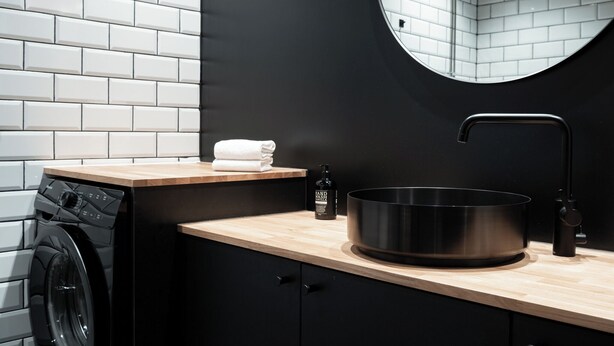 Una cocina moderna con un lavamanos de acero inoxidable, lavadora y encimera de madera.