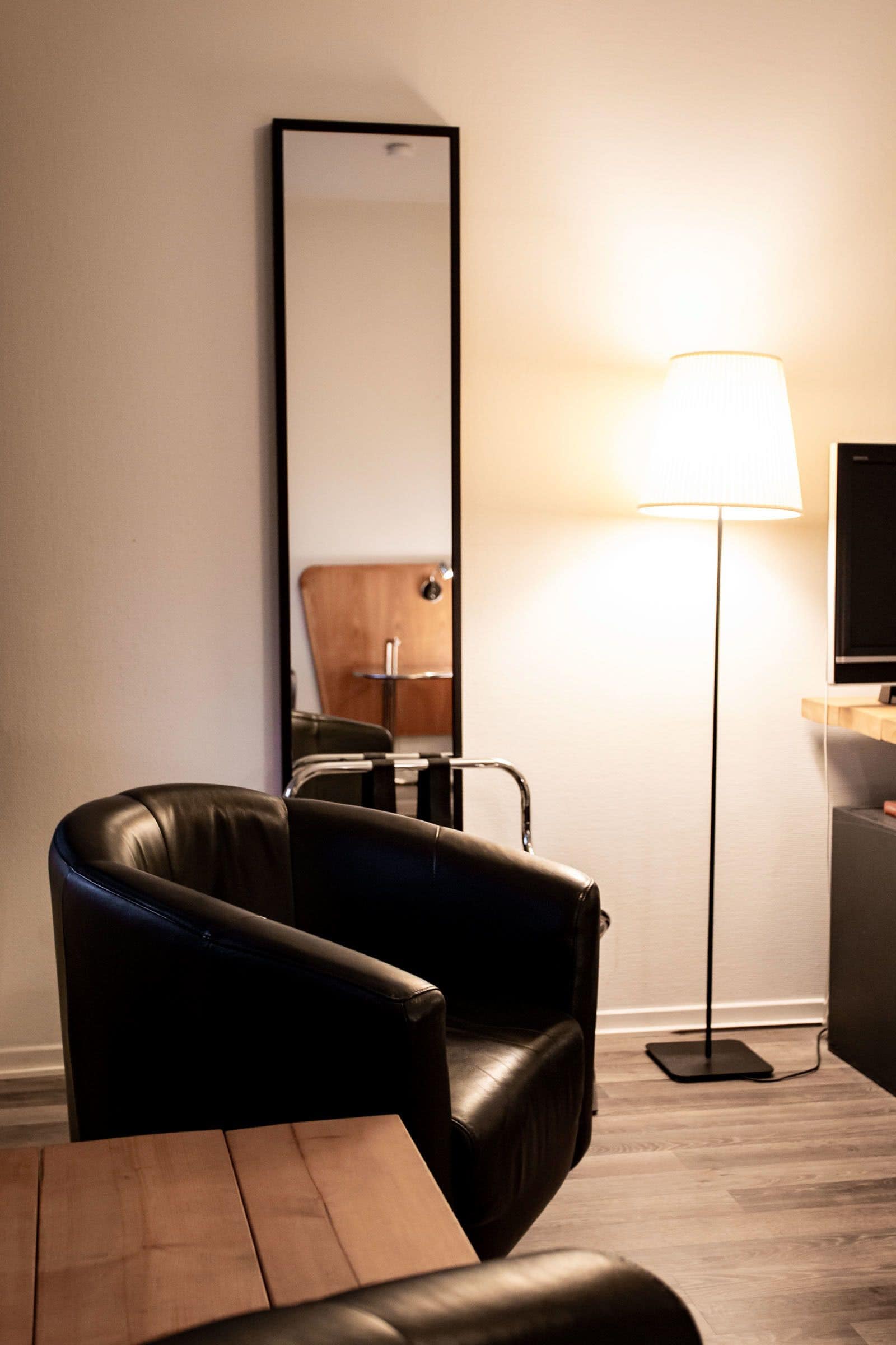 Una habitación moderna con un sillón de cuero, una mesa de madera, una lámpara de pie y un espejo grande en la pared.