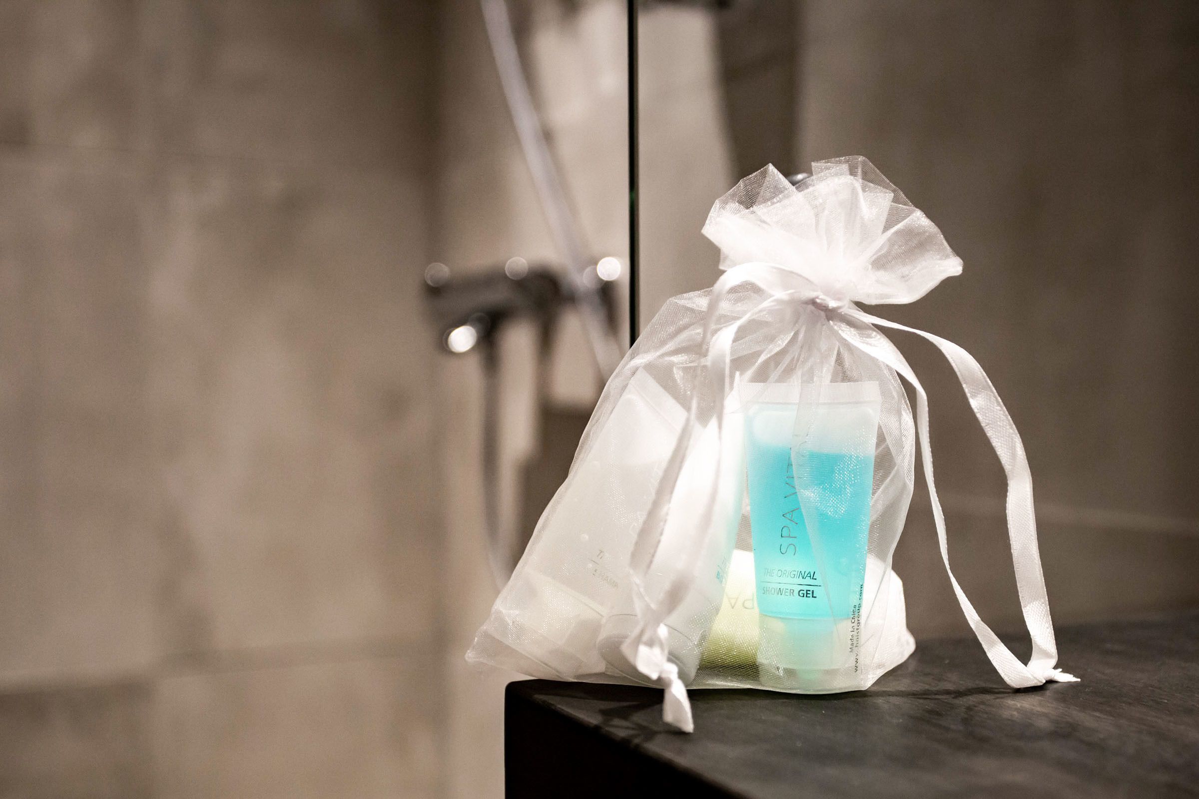A transparent gift bag with a ribbon, containing a bottle of SPA shower gel, placed on a dark surface.