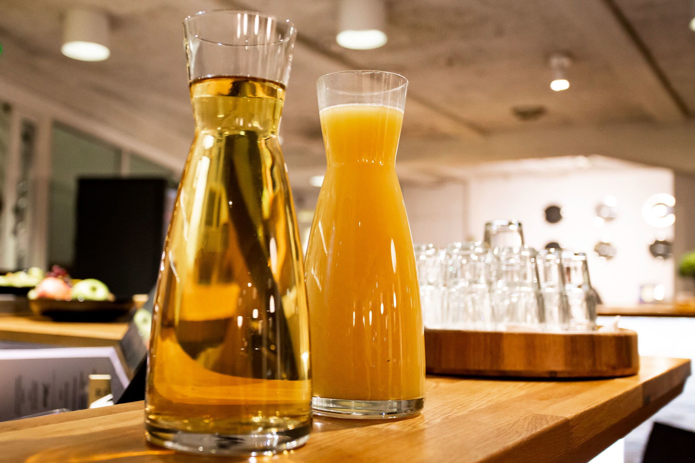 Un comptoir de bar en bois, avec une bouteille contenant un liquide ambré et un verre de jus d’orange.
