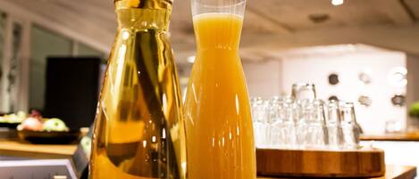 Un comptoir de bar en bois, avec une bouteille contenant un liquide ambré et un verre de jus d’orange.