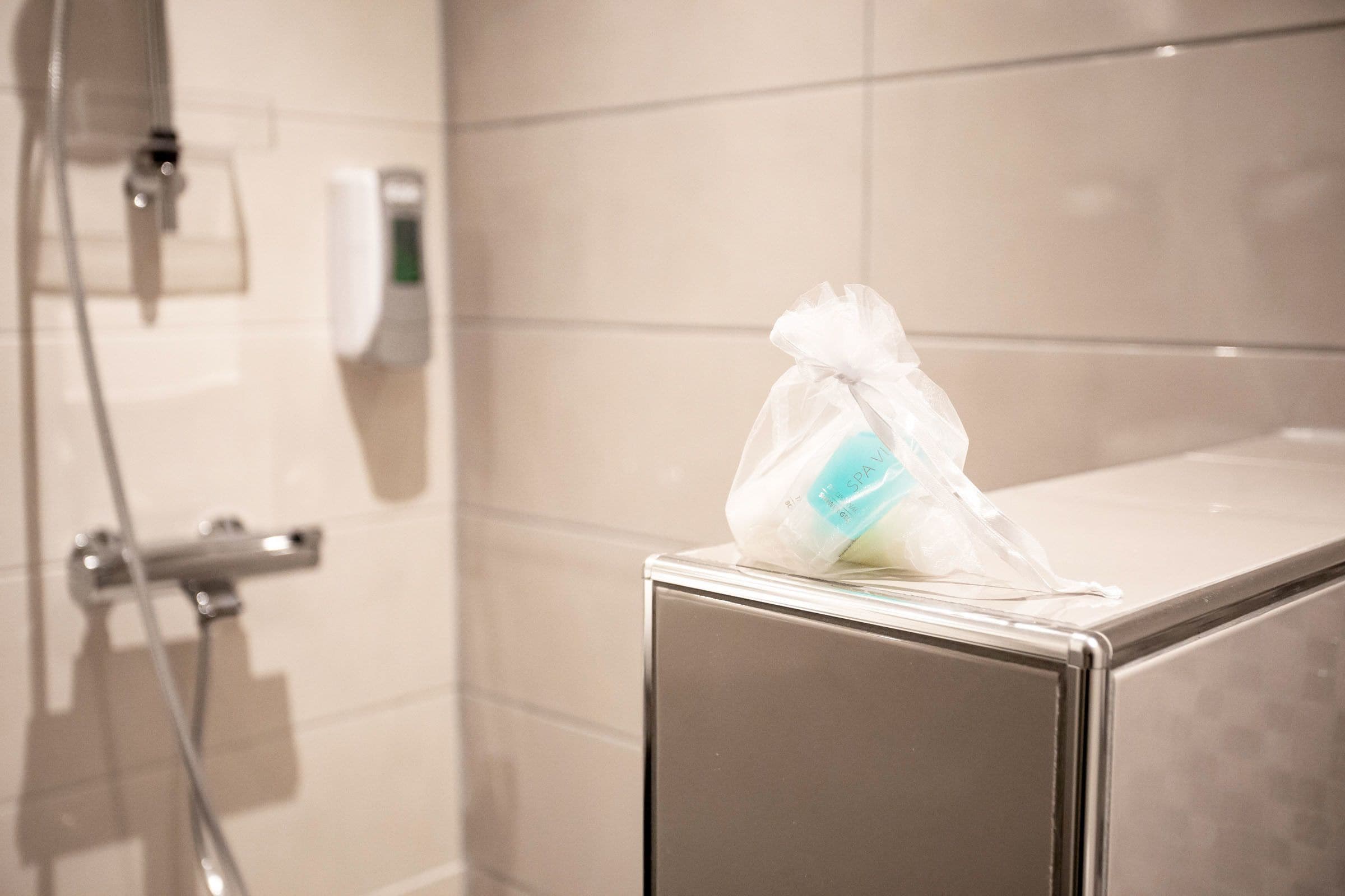 Un baño con ducha, dispensador de jabón y una bolsa de plástico sobre un mostrador.