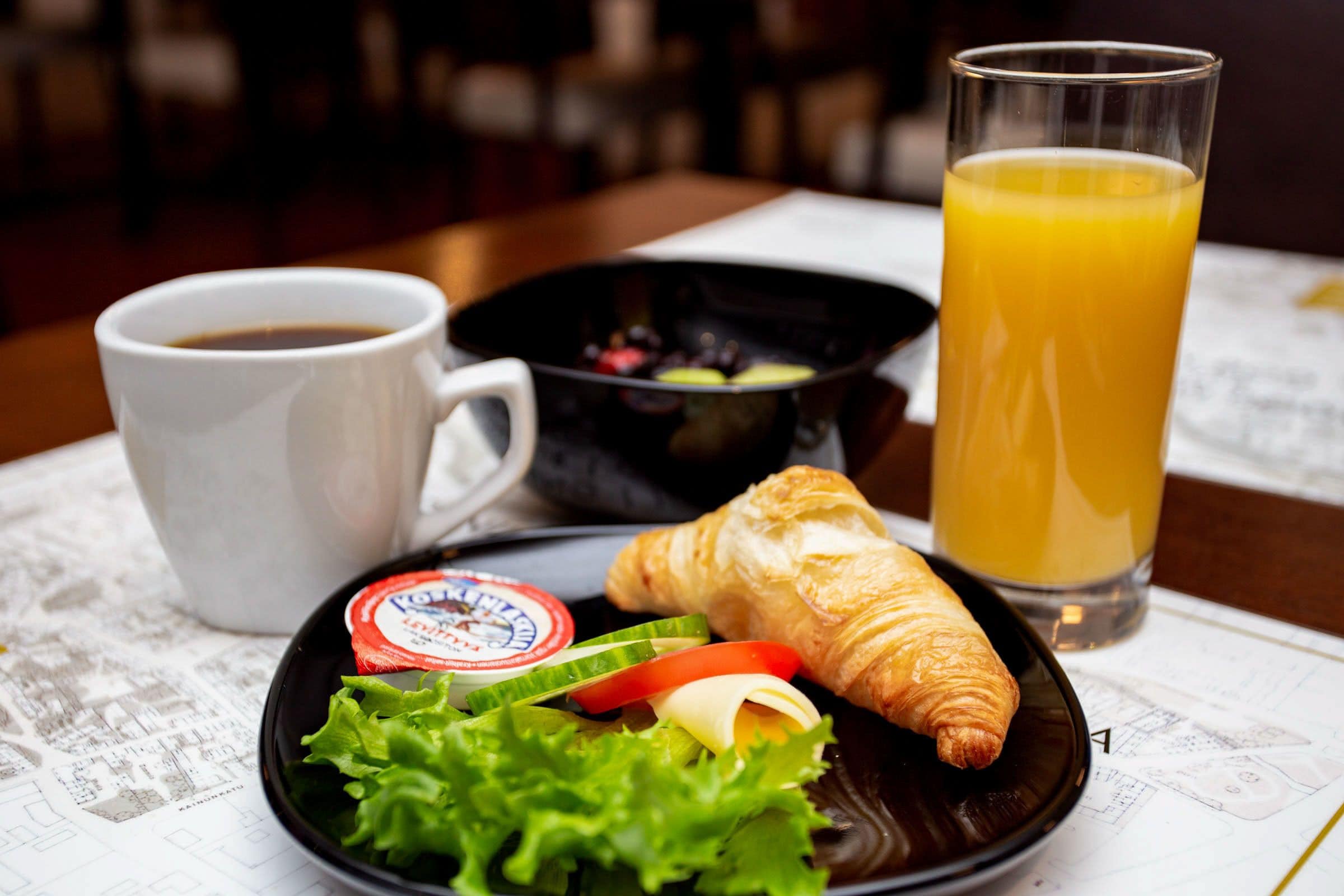 A breakfast setting with a croissant, a cup of coffee, a glass of orange juice, and a small salad on a table.