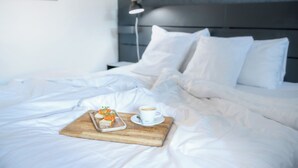 Una cama bien hecha con sábanas blancas, una bandeja de comida y una taza de café sobre una tabla de madera.