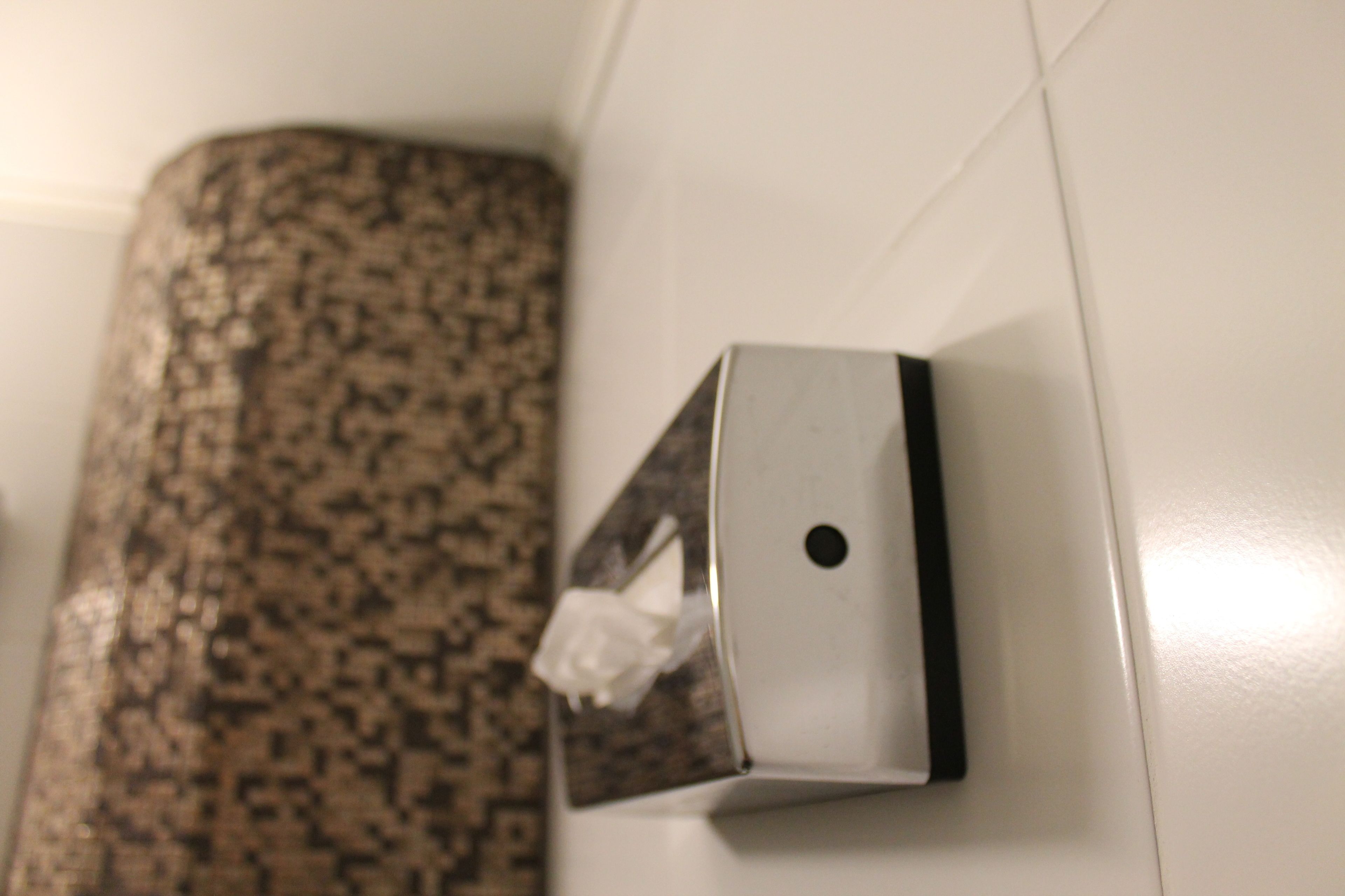Dispensador de pañuelos adherido a una pared con un rebozo de azulejos estampados.