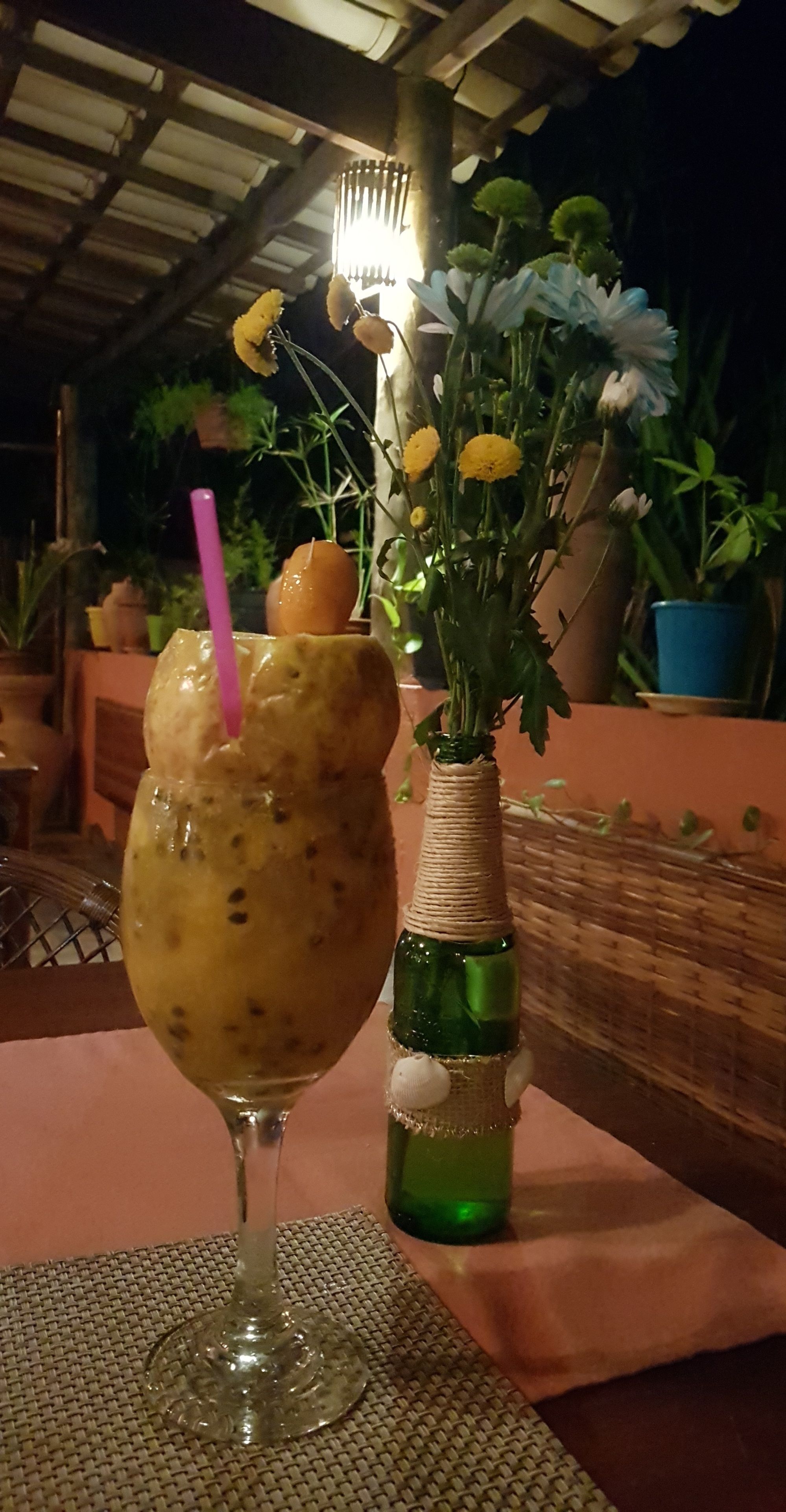 Une table avec un verre contenant une boisson, une bouteille et un vase de fleurs.