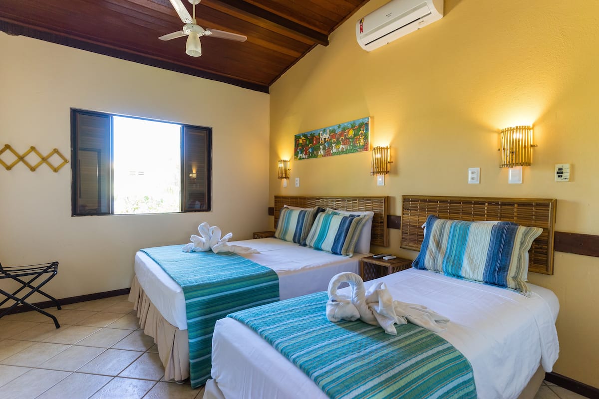 Une chambre d’hôtel avec deux lits, un ventilateur de plafond, un climatiseur et un tableau au mur.