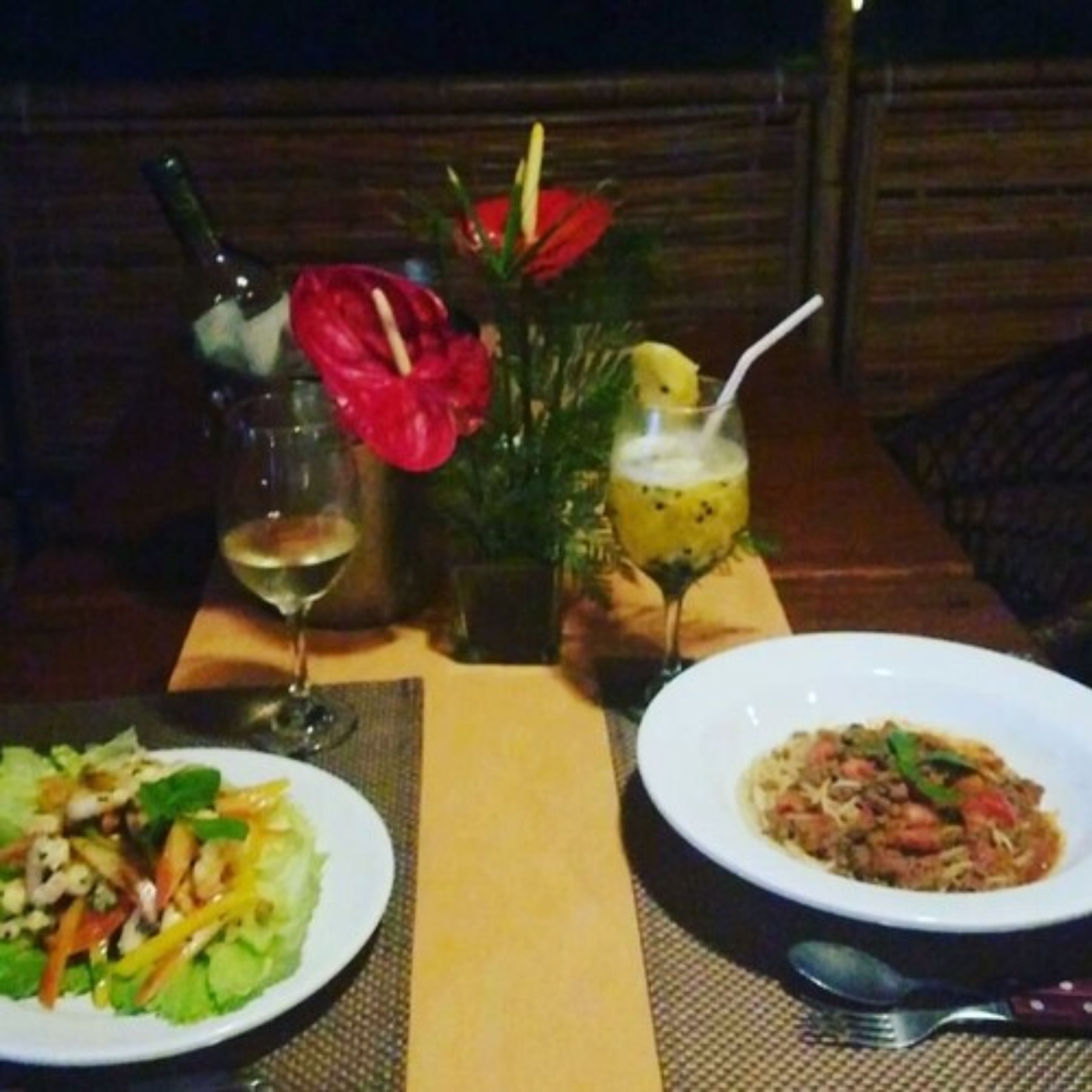 A dining table with a salad, a bowl of pasta, a glass of wine, and a cocktail with a pineapple garnish.