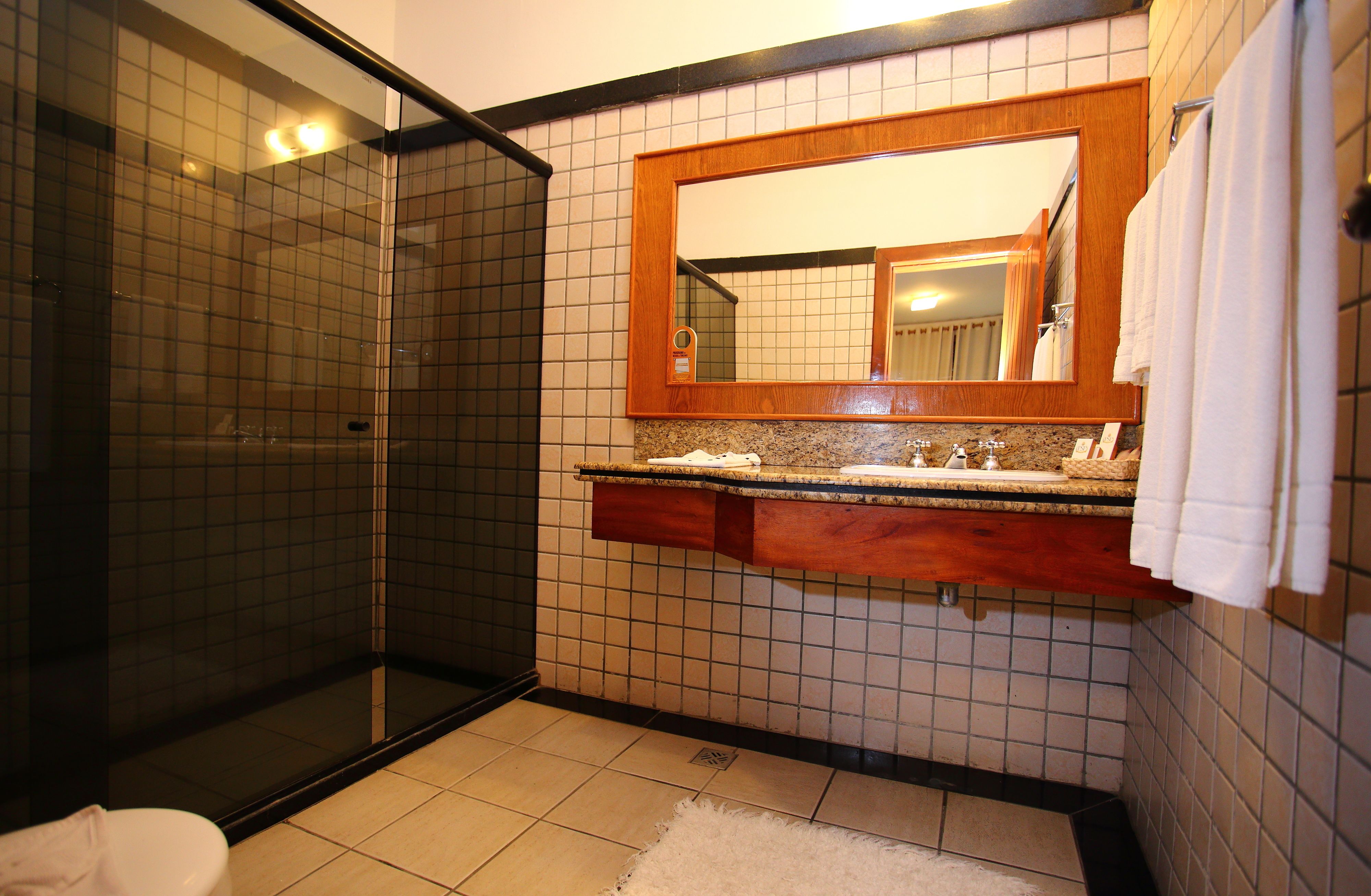 A bathroom with a glass-enclosed shower, a wooden vanity with a mirror, and tiled walls.