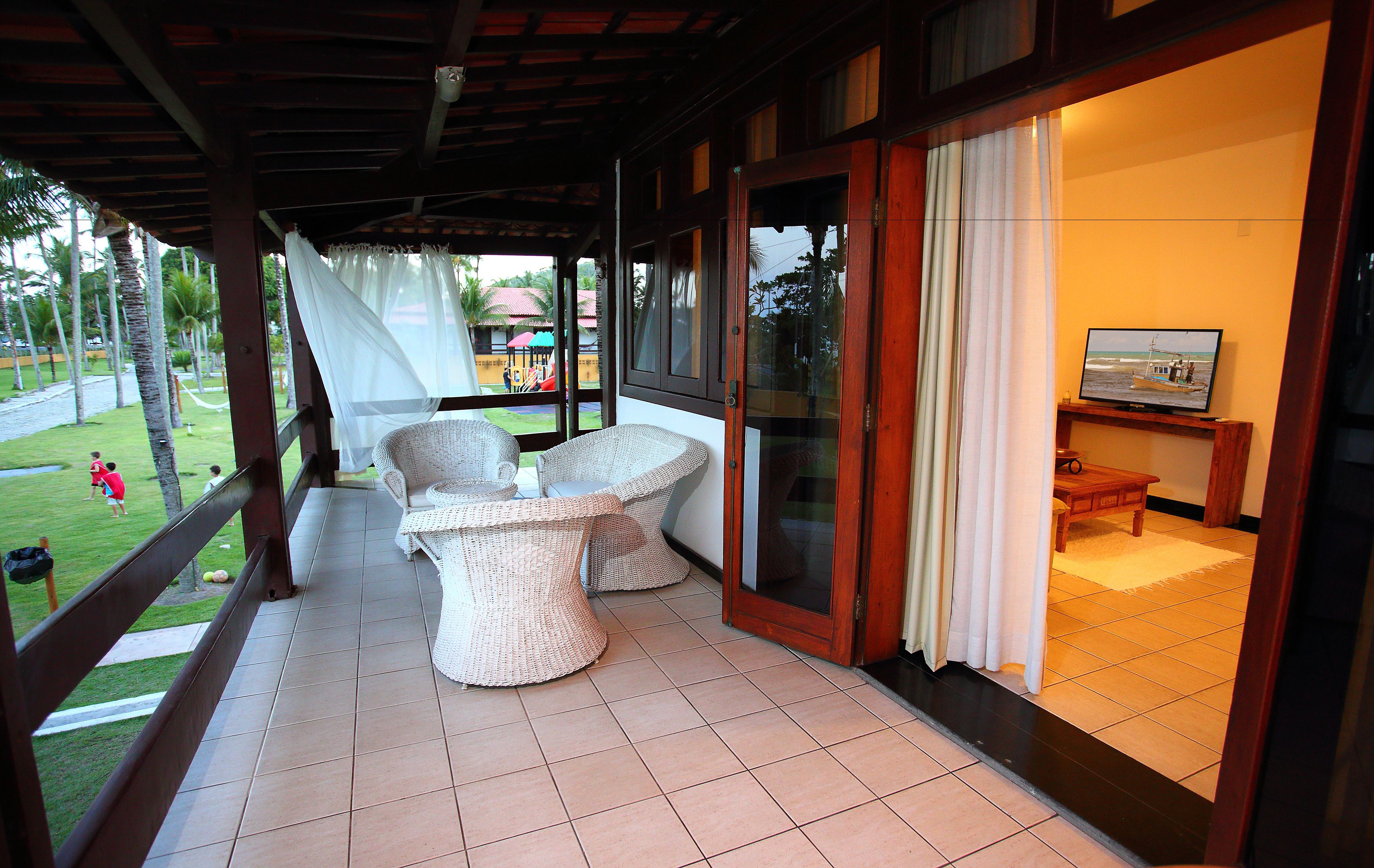 A covered outdoor seating area with wicker furniture and a television in the background.
