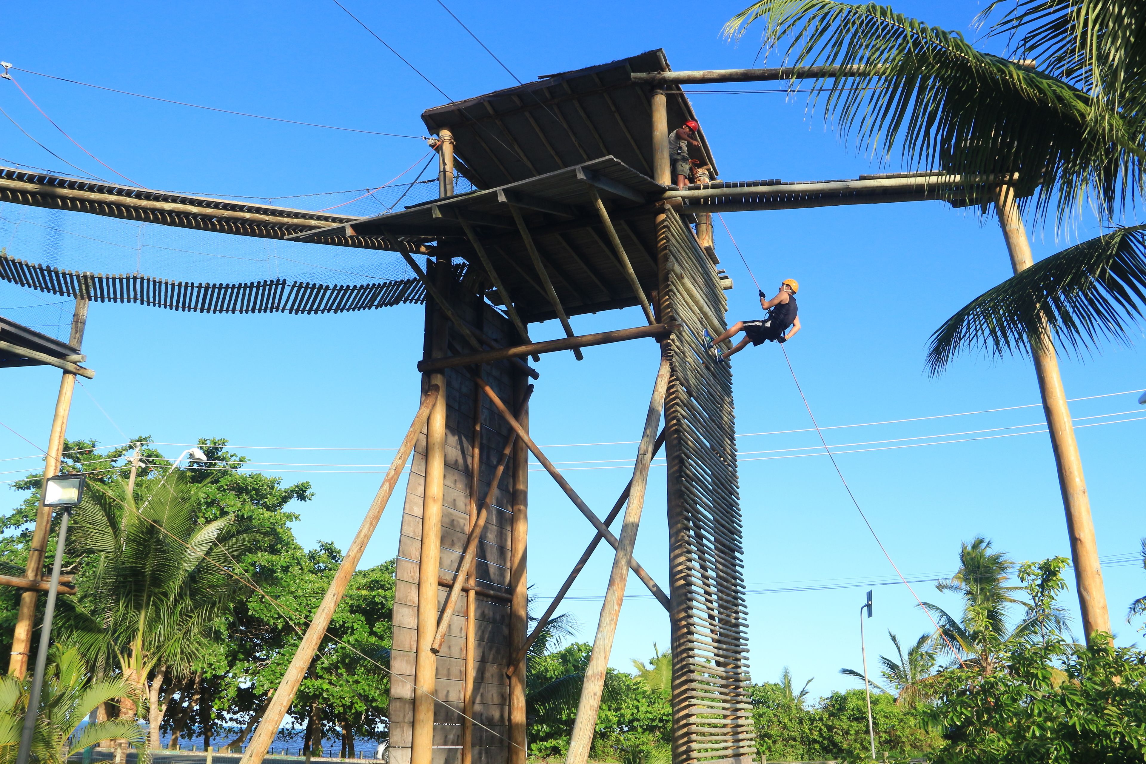 A wooden structure with a rope bridge and a person climbing it.