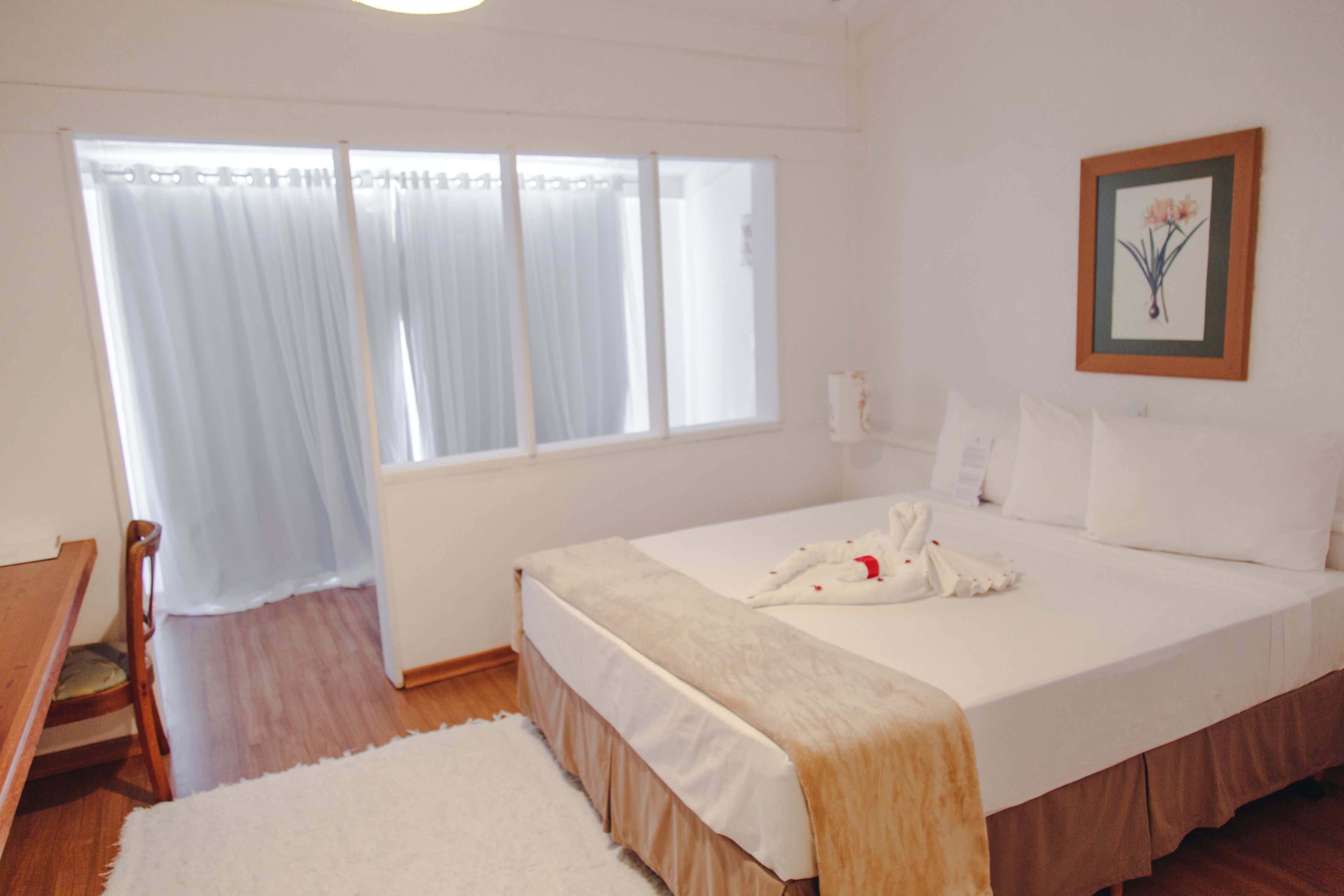 Quarto de hotel com cama, uma cadeira, janela com cortinas e um quadro na parede.