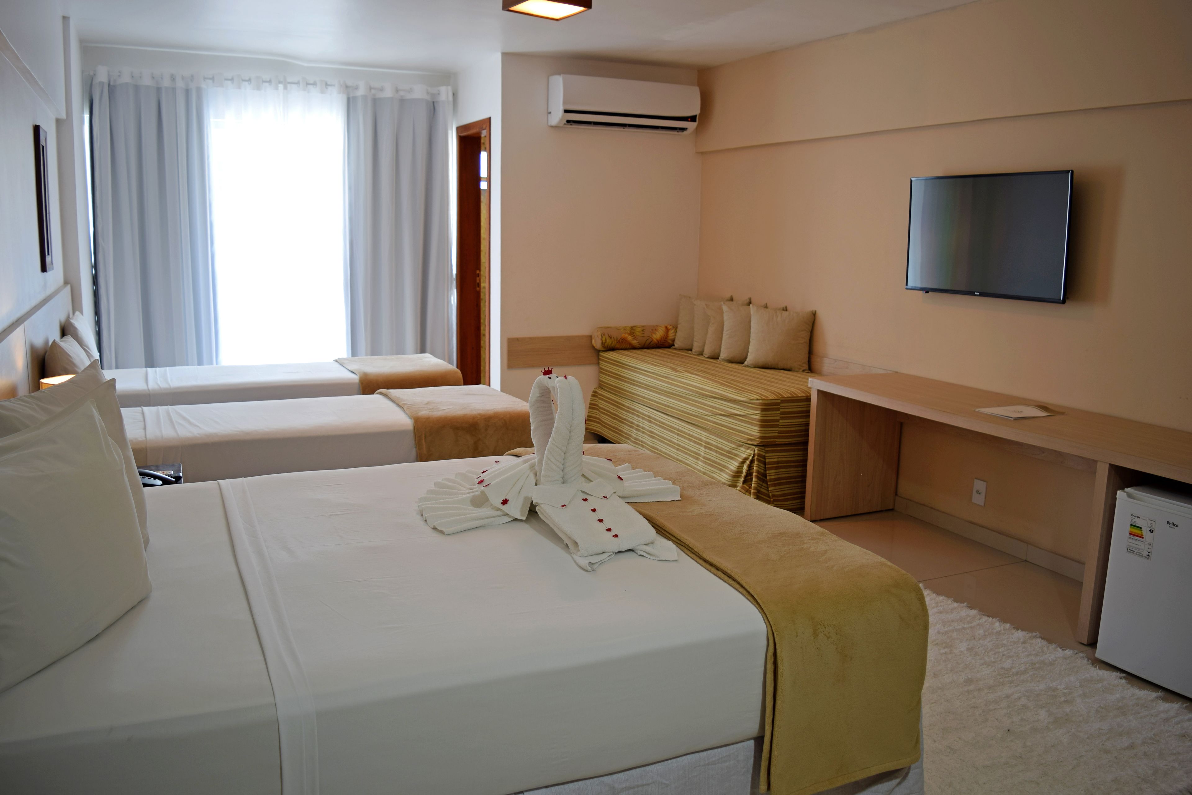 A hotel room with two beds, a TV, a desk, and a small refrigerator.