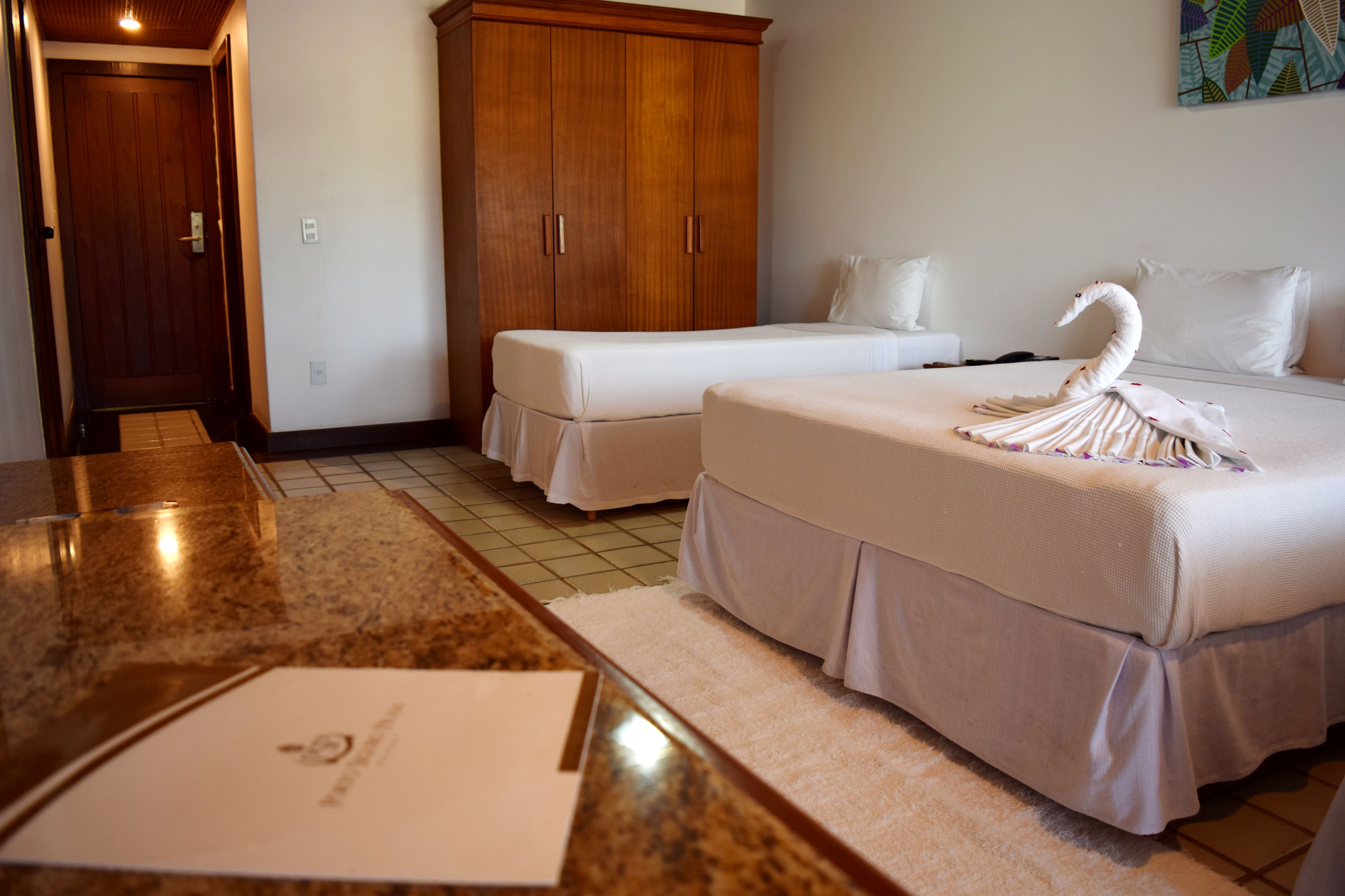 Quarto de hotel com duas camas, um guarda-roupa de madeira, bancada de mármore e toalha em formato de cisne.