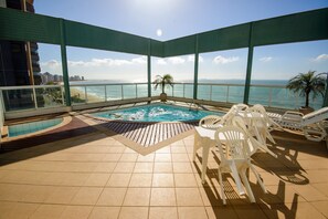 Una piscina en la azotea con vista al océano, rodeada de sillones de descanso y una palmera.