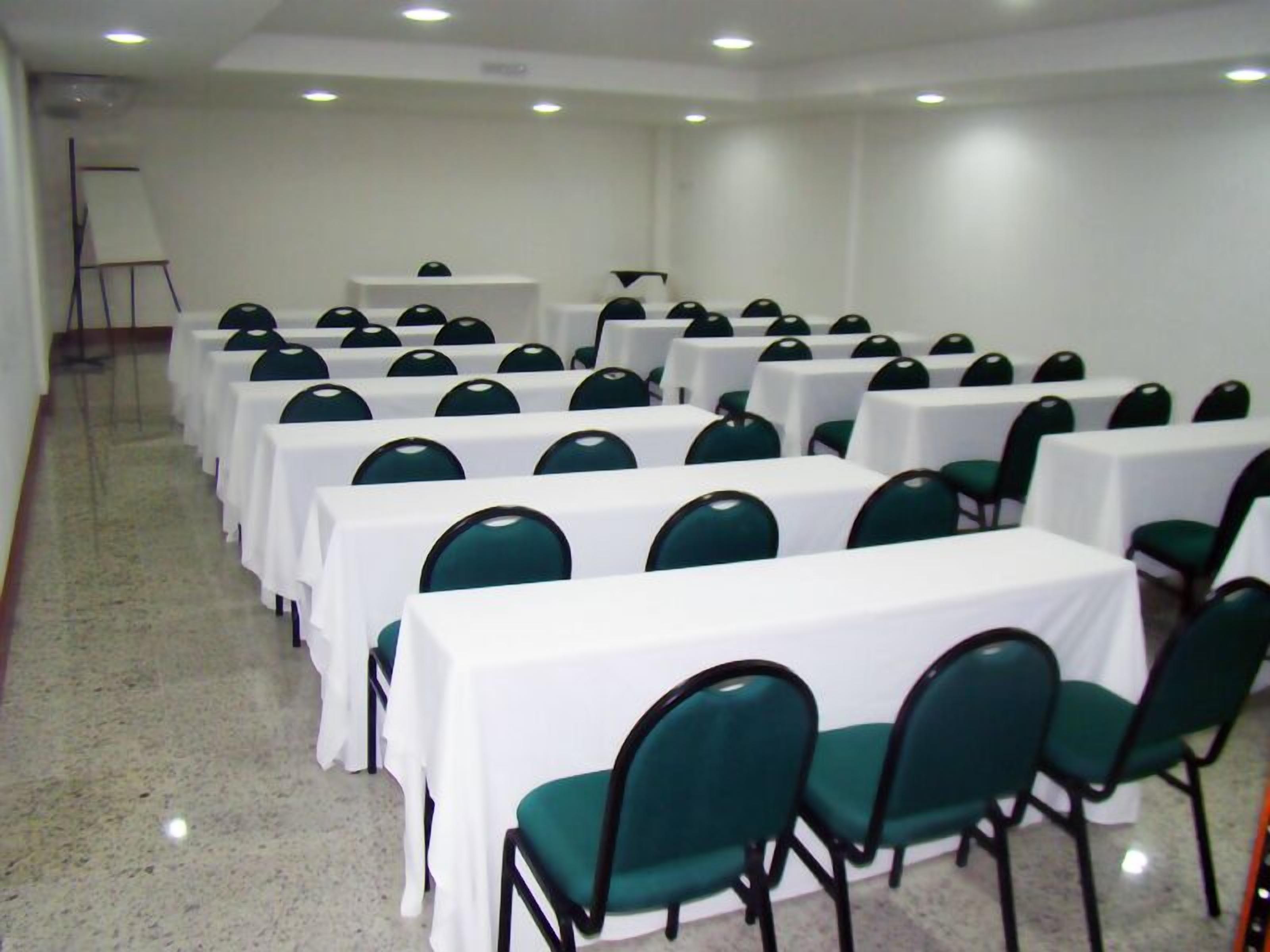 Un salón de conferencias con filas de mesas y sillas, una pizarra y un proyector.