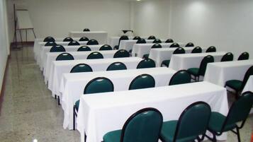 Un salón de conferencias con filas de mesas y sillas, una pizarra y un proyector.