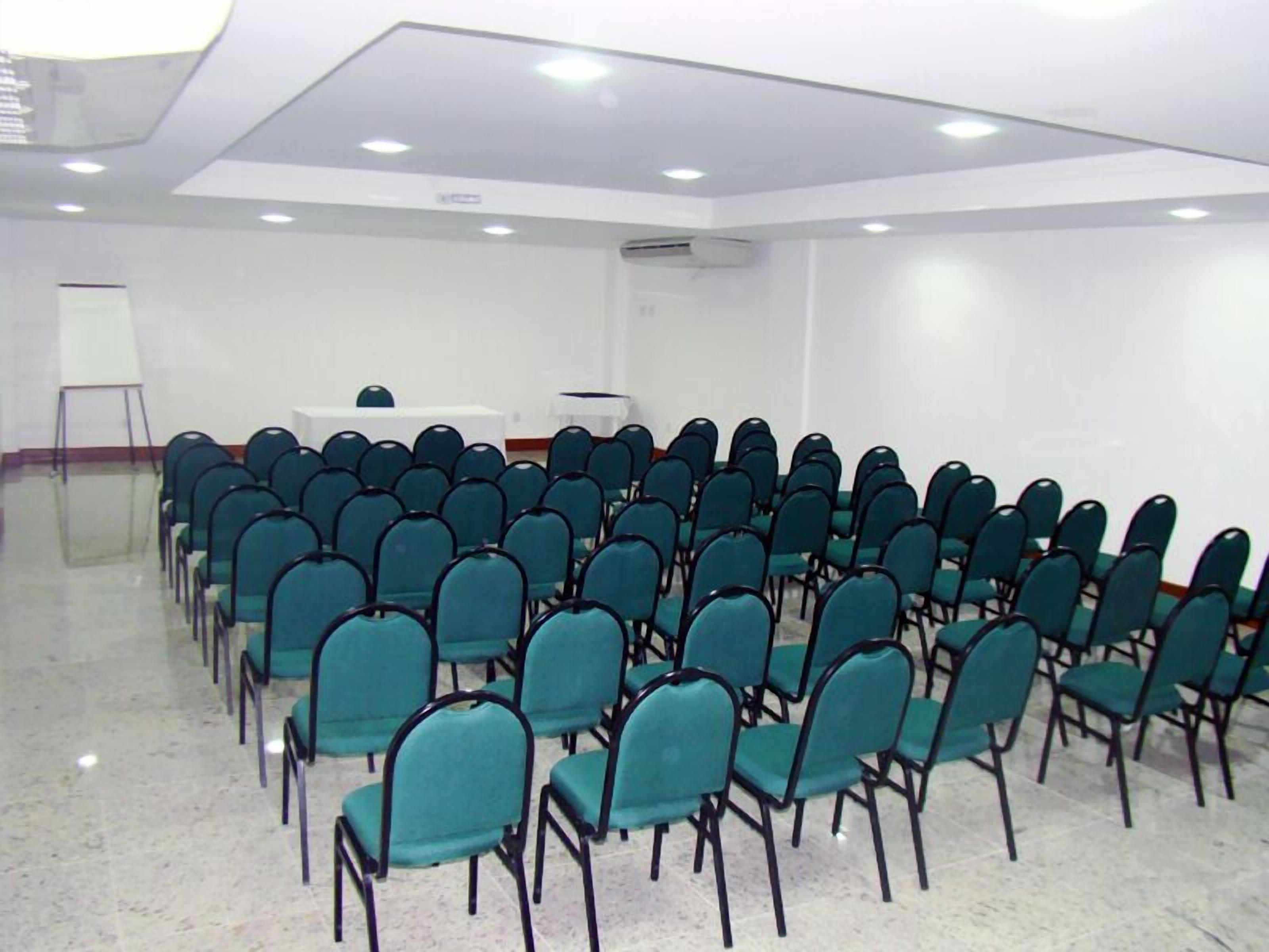 A conference room with rows of teal chairs, a whiteboard, and a podium.