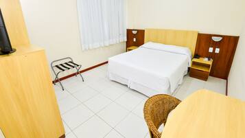 Una habitación de hotel con cama, una mesita, una silla, televisor y ventana con cortinas.
