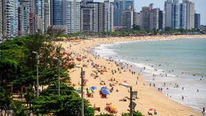 Una playa con un paisaje urbano al fondo, con edificios altos y una orilla arenosa con sombrillas.