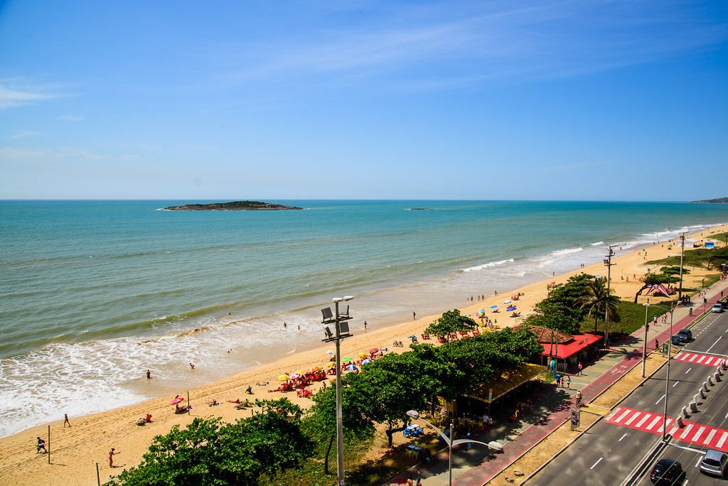 A beach with people, umbrellas, and a road with vehicles.