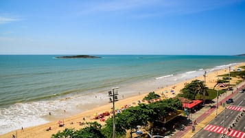 A beach with people, umbrellas, and a road with vehicles.