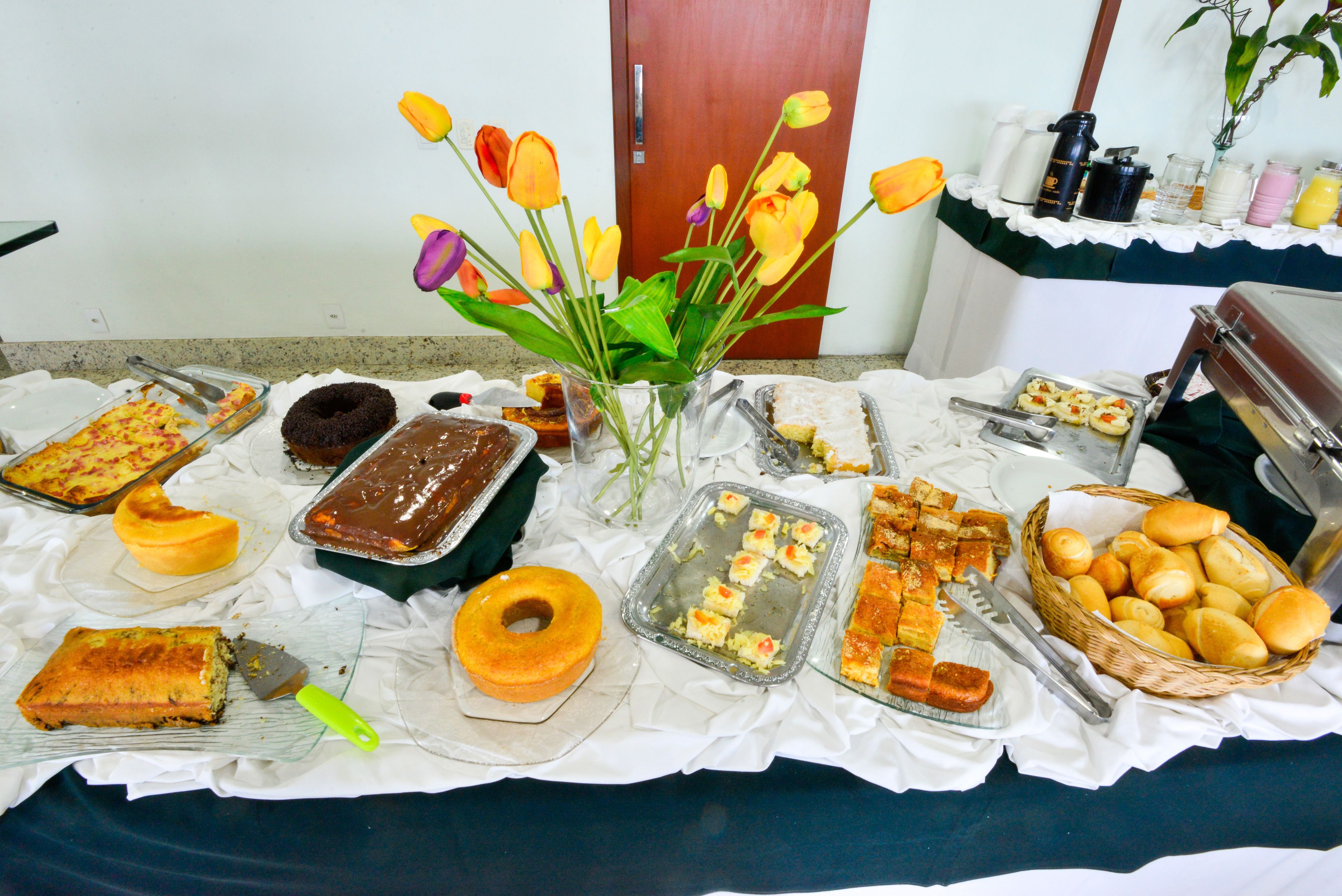 A buffet table with various food items, including cakes, pastries, and a vase of flowers.