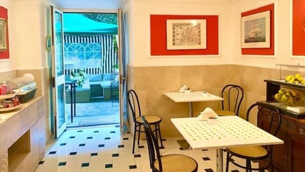 A dining area with a table and chairs, a kitchen counter with fruit, and a view of the outside. - Hotel Actor (Genoa)