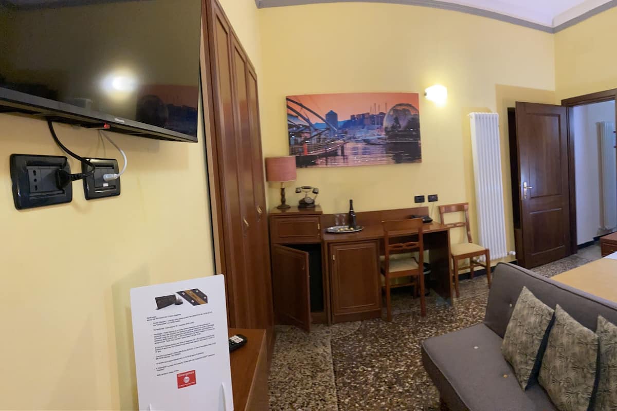 A hotel room with a bed, a sofa, a desk with a chair, a television, and artwork on the walls.