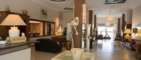 Un espace d’accueil comprenant un comptoir de réception, une table de billard et un coin salon avec un canapé et des fauteuils.