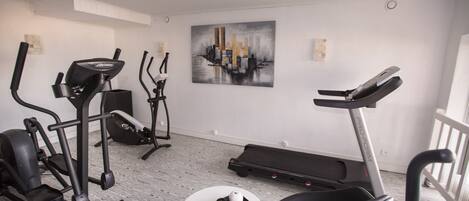 Un gimnasio en casa con diverso equipo de ejercicio, incluyendo una caminadora, elíptica y bicicleta estática.