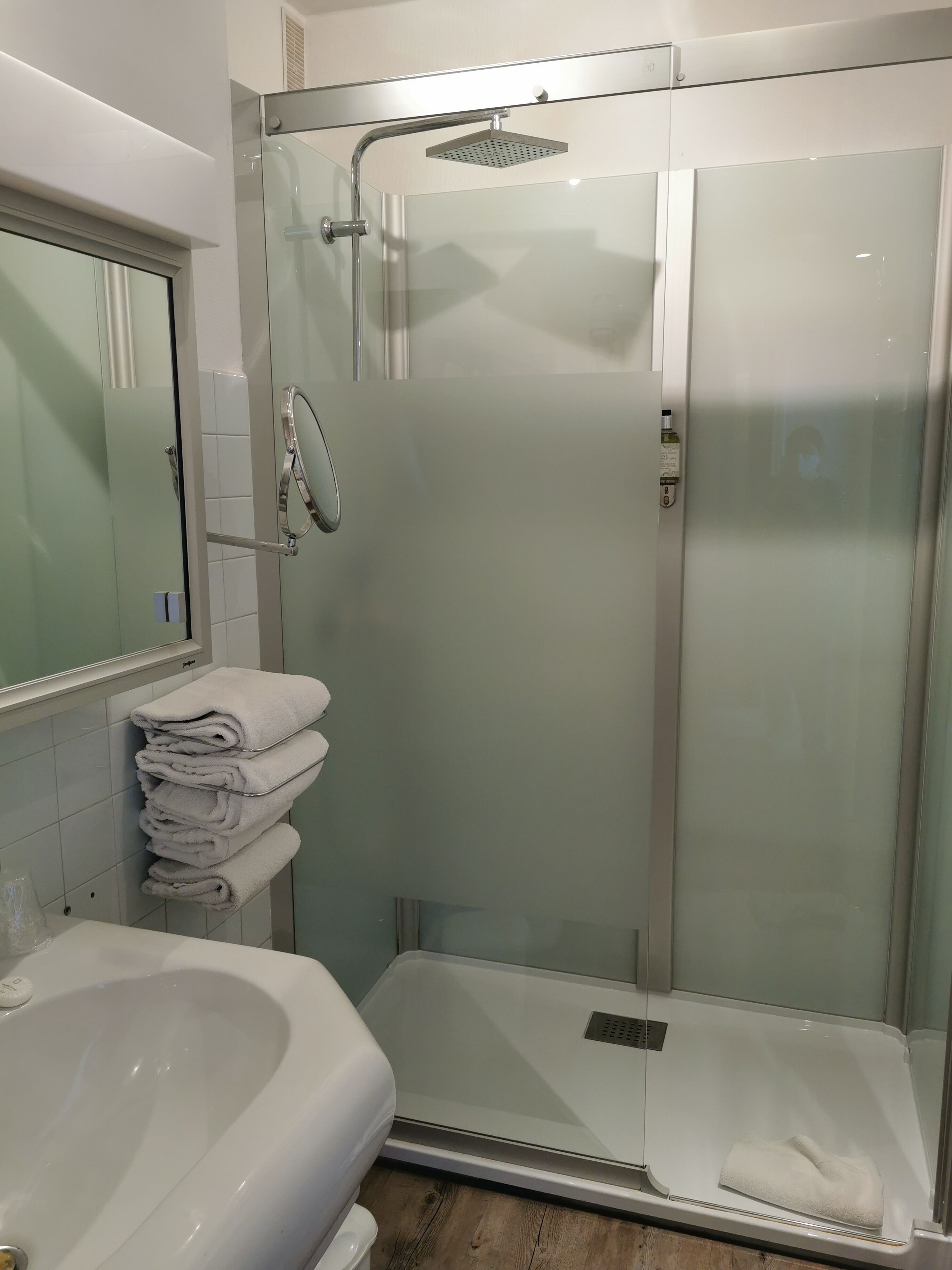 A modern bathroom with a glass-enclosed shower, a white bathtub, and a stack of white towels on a rack.
