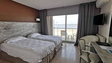Een hotelkamer met twee bedden, een bureau, een stoel, een televisie en uitzicht op het strand.