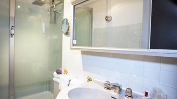 Un baño moderno con cabina de ducha de vidrio, un espejo grande y un lavabo blanco con dos grifos.