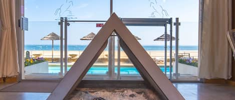 Un área de piscina moderna con diseño geométrico, vista despejada de la playa y el océano, y una puerta de vidrio que da a la piscina.