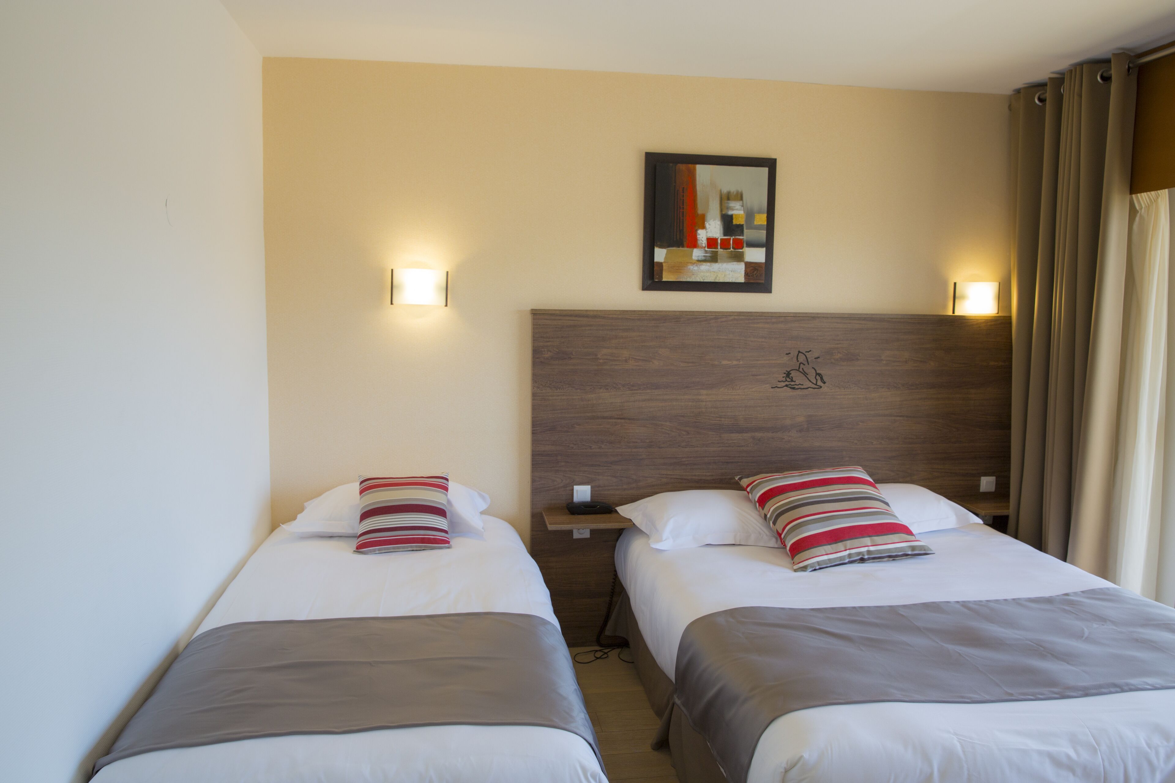 Habitación de hotel con dos camas, cada una con una almohada y una mesita de noche. Hay una lámpara de pared sobre las camas y un cuadro en la pared.