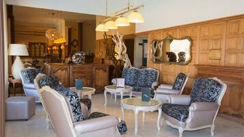 A spacious lobby with elegant furniture, including patterned armchairs and a sofa, a wooden reception desk, and a chandelier.