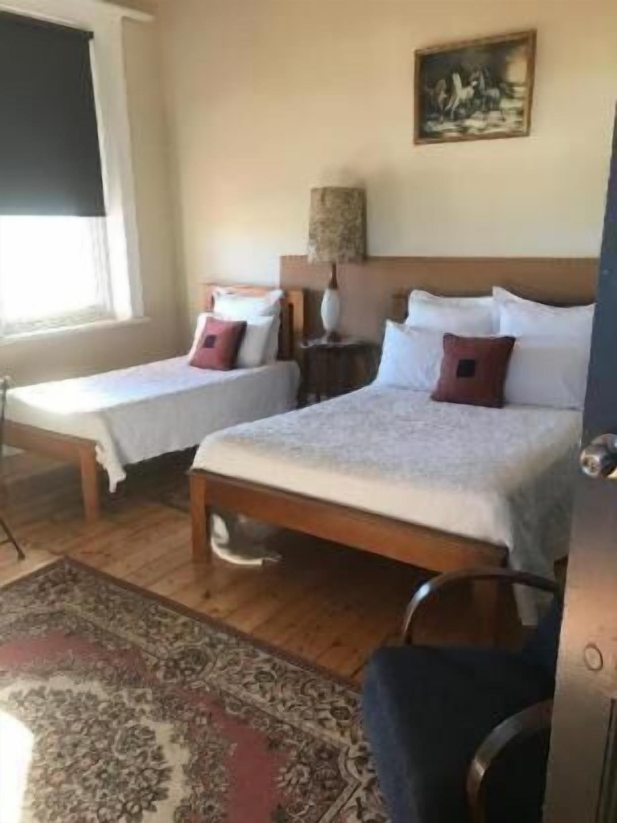 A double room with two single beds, a wooden floor, a patterned rug, and a painting on the wall.