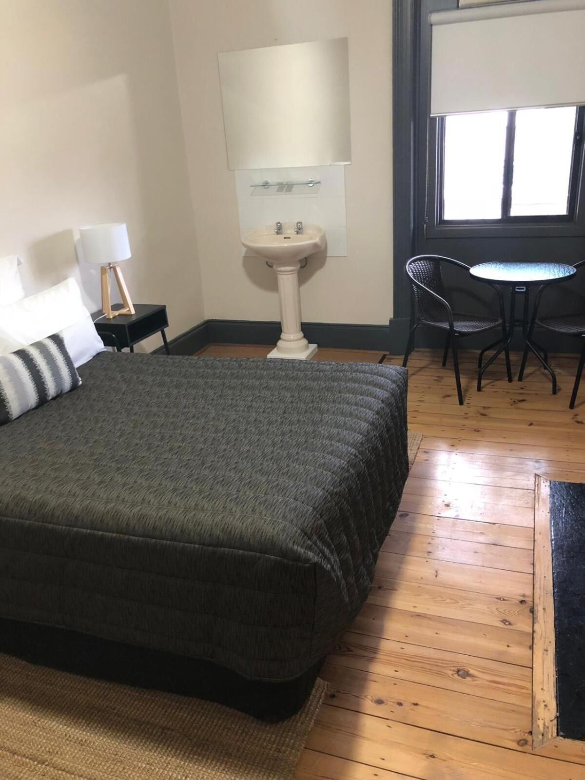 Ein Zimmer mit einem Bett, einem kleinen Tisch mit zwei Stühlen, einem Waschbecken und einem Fenster mit Jalousien.