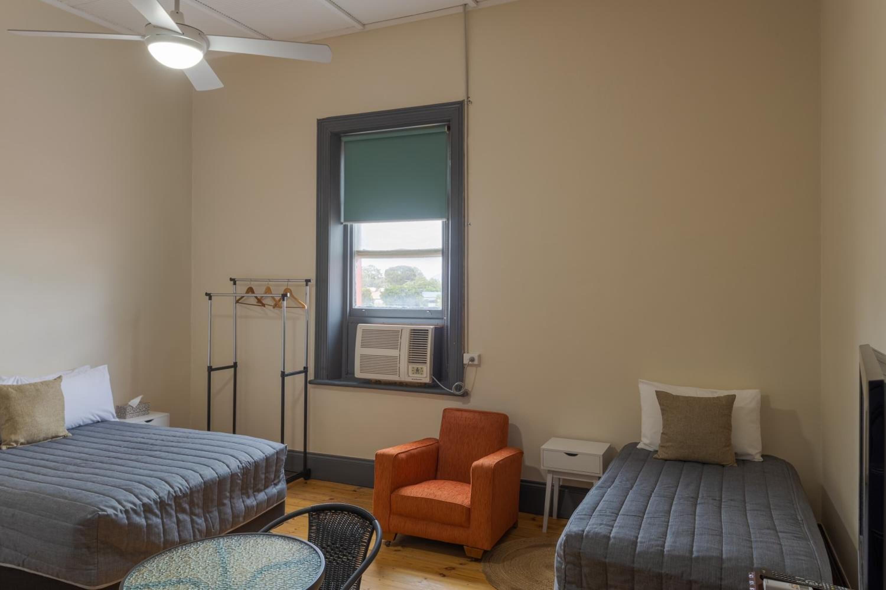 A bedroom with two beds, a ceiling fan, an air conditioning unit, a chair, and a small table.