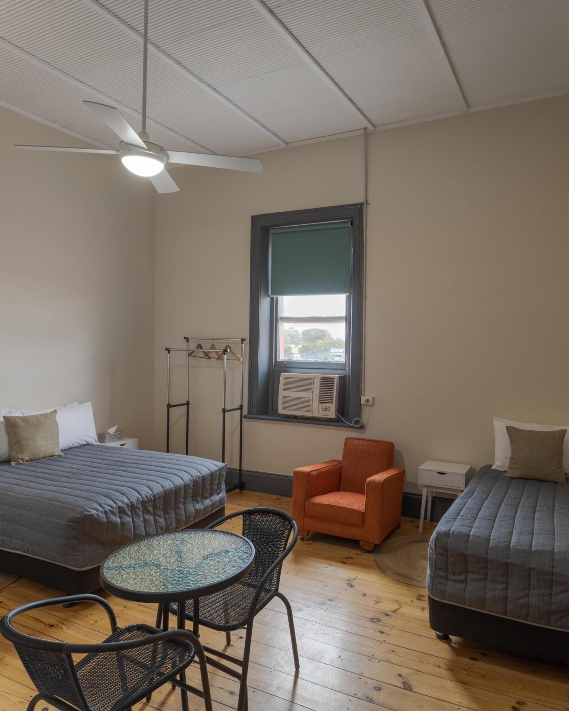 Une chambre de dortoir avec deux lits, une chaise, une table et un ventilateur de plafond.