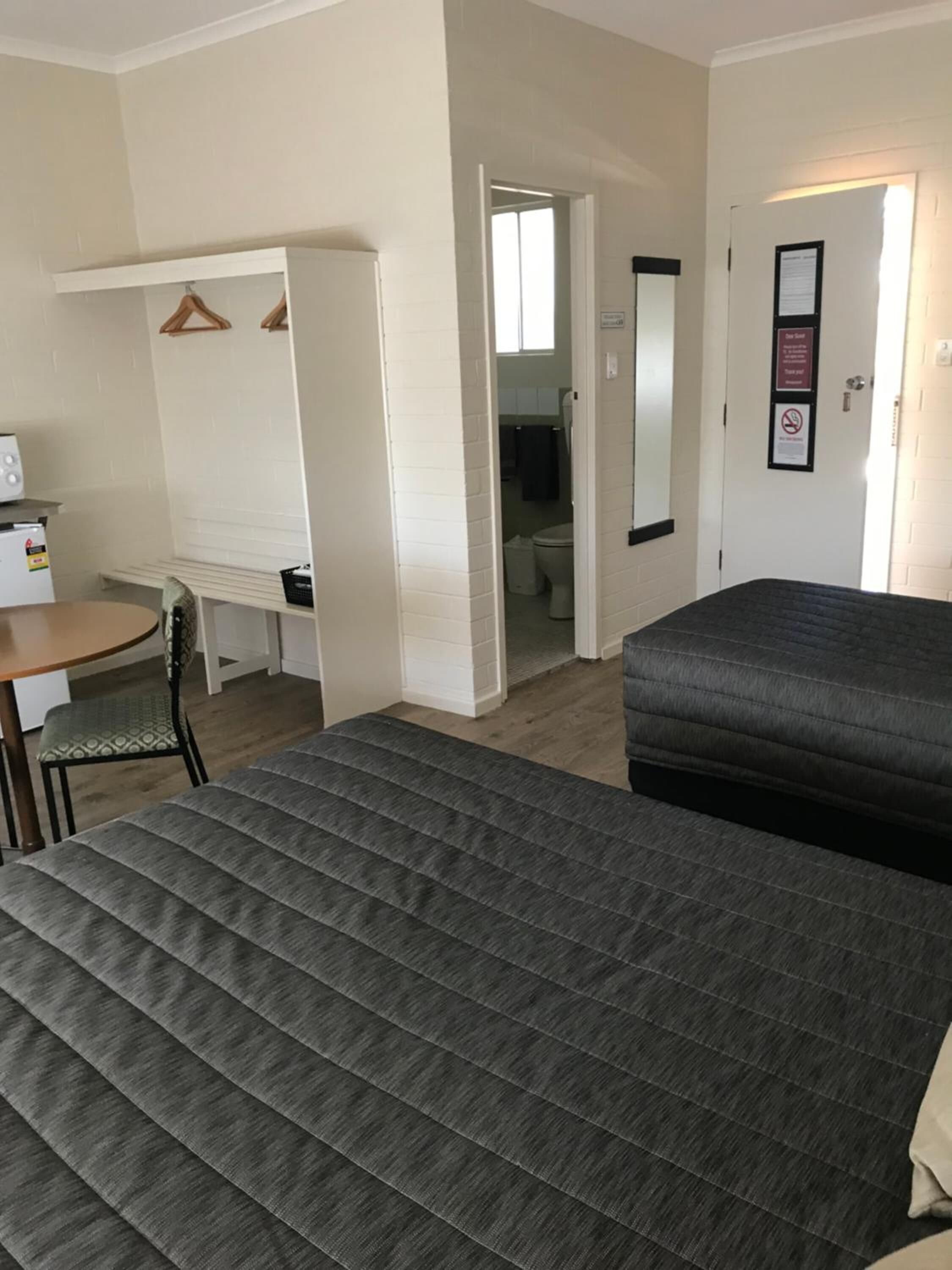 A room with a bed, a desk, and a chair. There is a door leading to a bathroom.