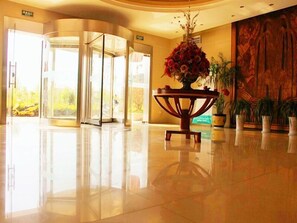 A lobby with a polished floor, a central table with a floral arrangement, and a large wooden wall with a mural. - GreenTree Inn Nantong Rugao Port Bus Station Business Hotel (Nantong)