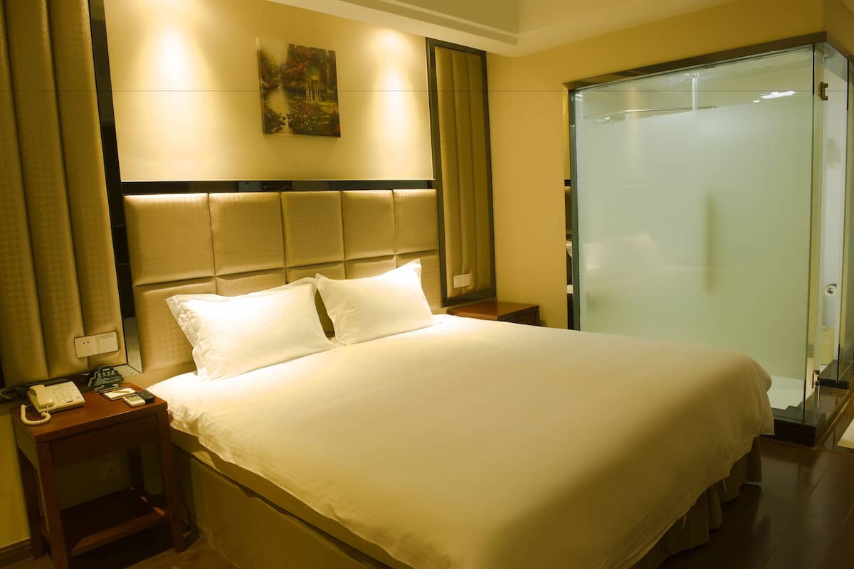 A hotel room with a large bed, a bedside table with a telephone, and a glass-enclosed shower.